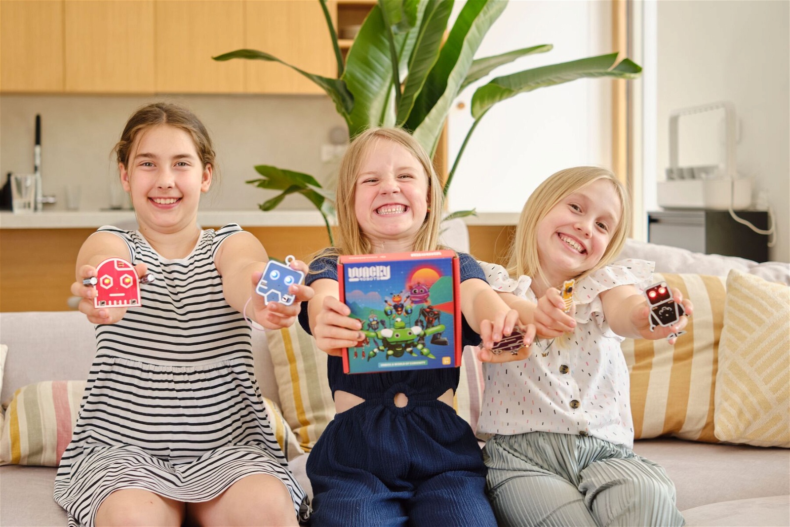 Troje dzieci siedzą uśmiechnięci na sofie i trzymają zestaw edukacyjny Dusty the Wacky Robot.